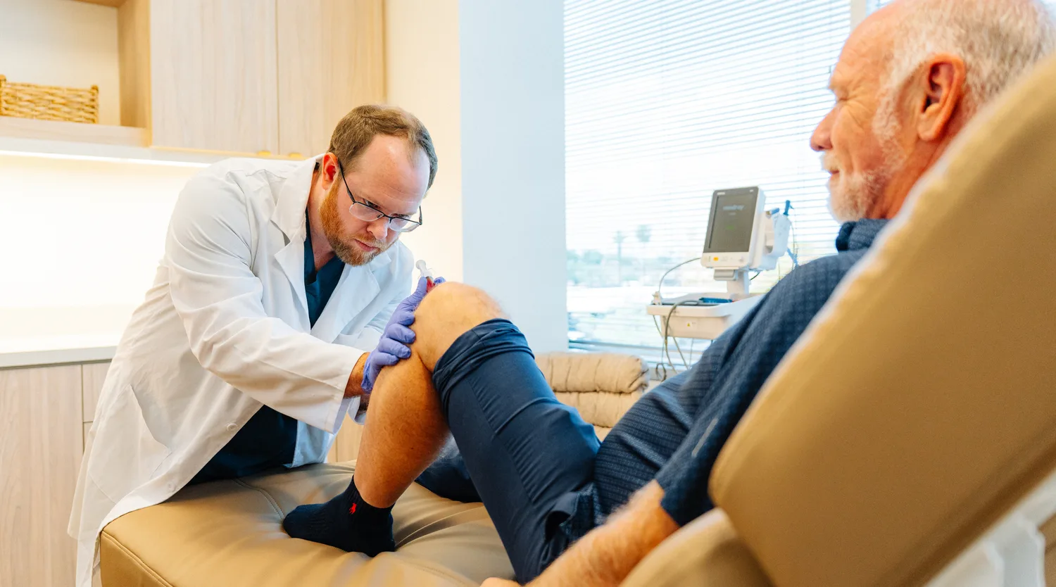 A doctor treating an older man’s knee as he reclines in a treatment chair