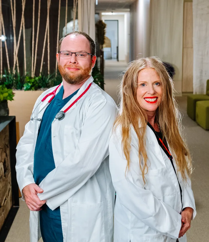 Dr. Sharon Stills and Dr. Ben Stills in white coats, standing back to back in a clinic corridor