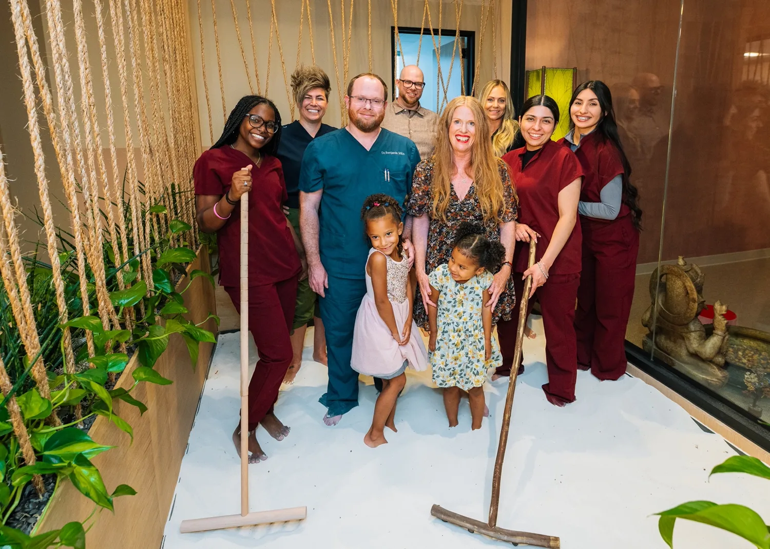 The center’s team in scrubs and casual clothes with two young girls, standing barefoot in an indoor white-sand garden