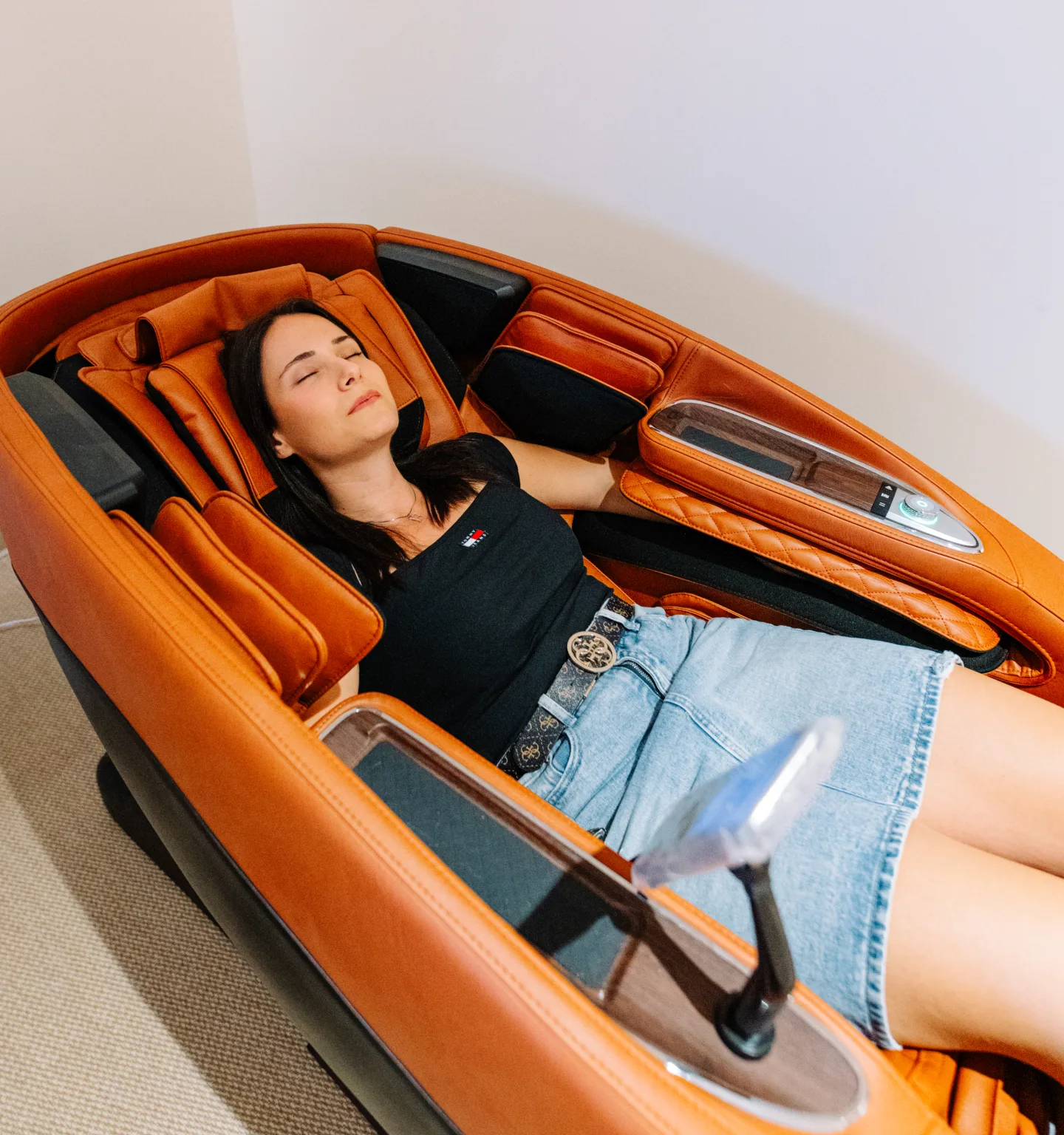 A woman reclines with her eyes closed in an orange and black full-body massage chair